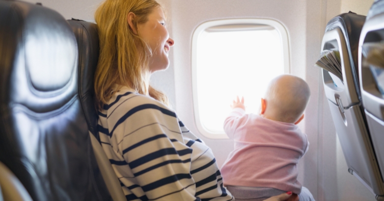 A woman holds a baby while seated on an airplane, illustrating family travel tips for entertaining children during flights.