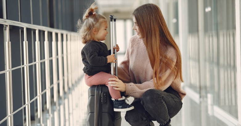 A woman and child are seated on a suitcase, representing air travel tips for families with children during security checks.